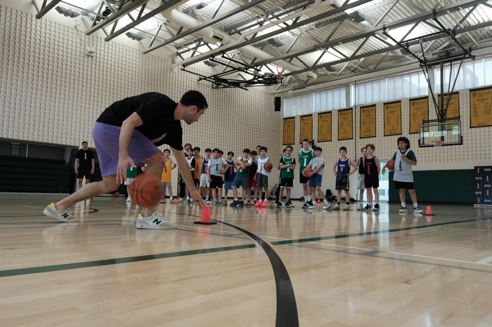 A 3BA coach demonstrating a low dribble in front of a full gym of students