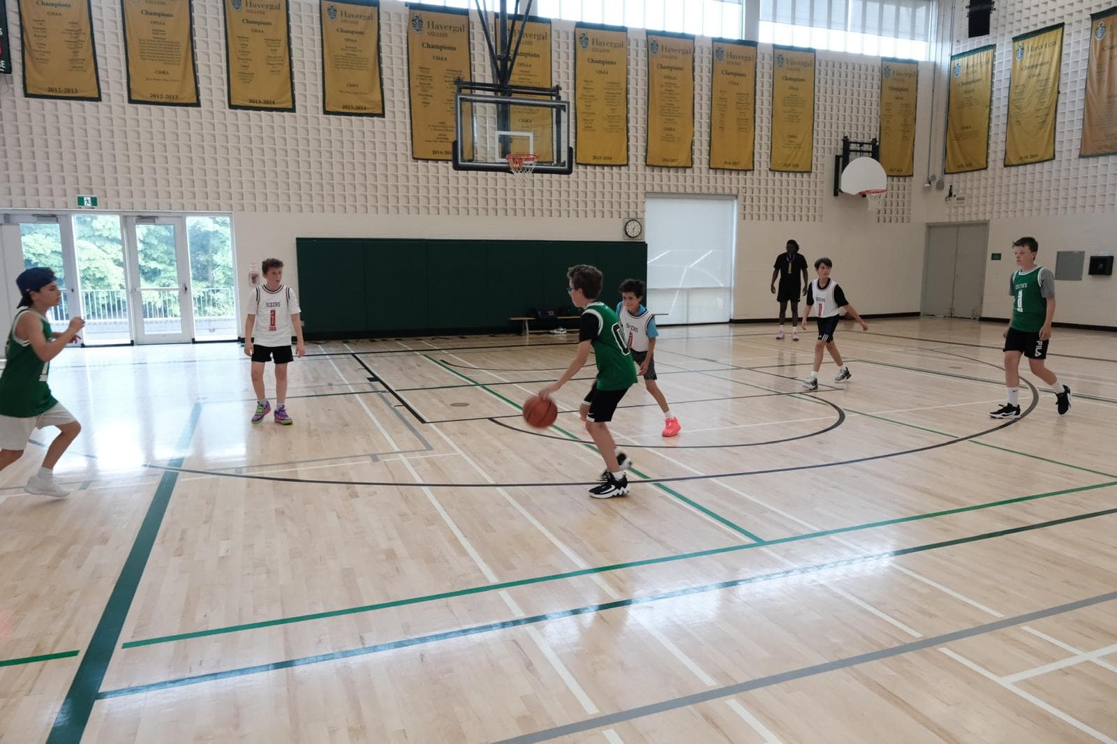 A wide 3x3 game in a bright gym with players spread across the floor