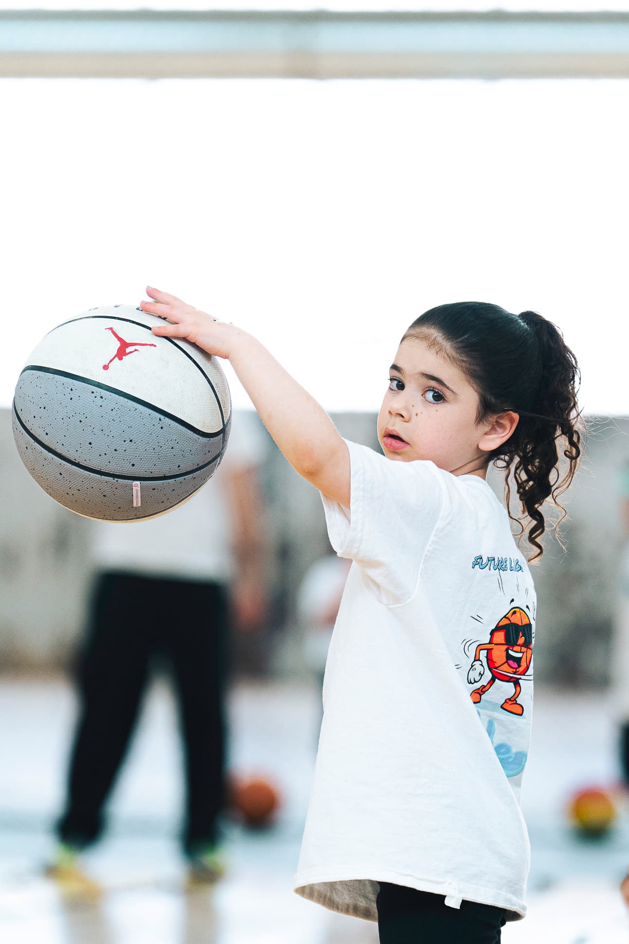 A young Next Gen athlete holding a basketball up in one hand, ready to shoot
