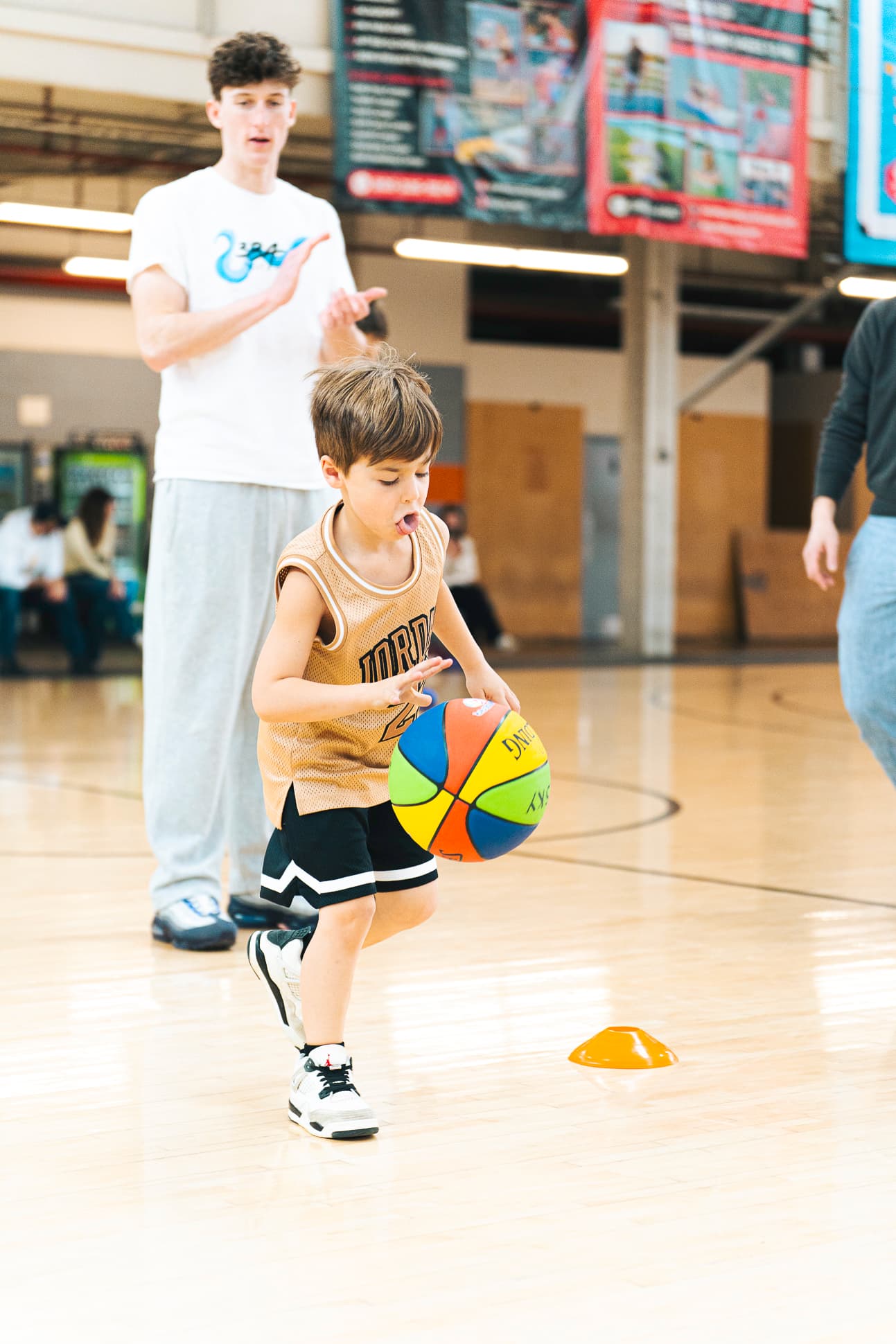 A young athlete dribbling toward a cone while a 3BA coach cheers him on