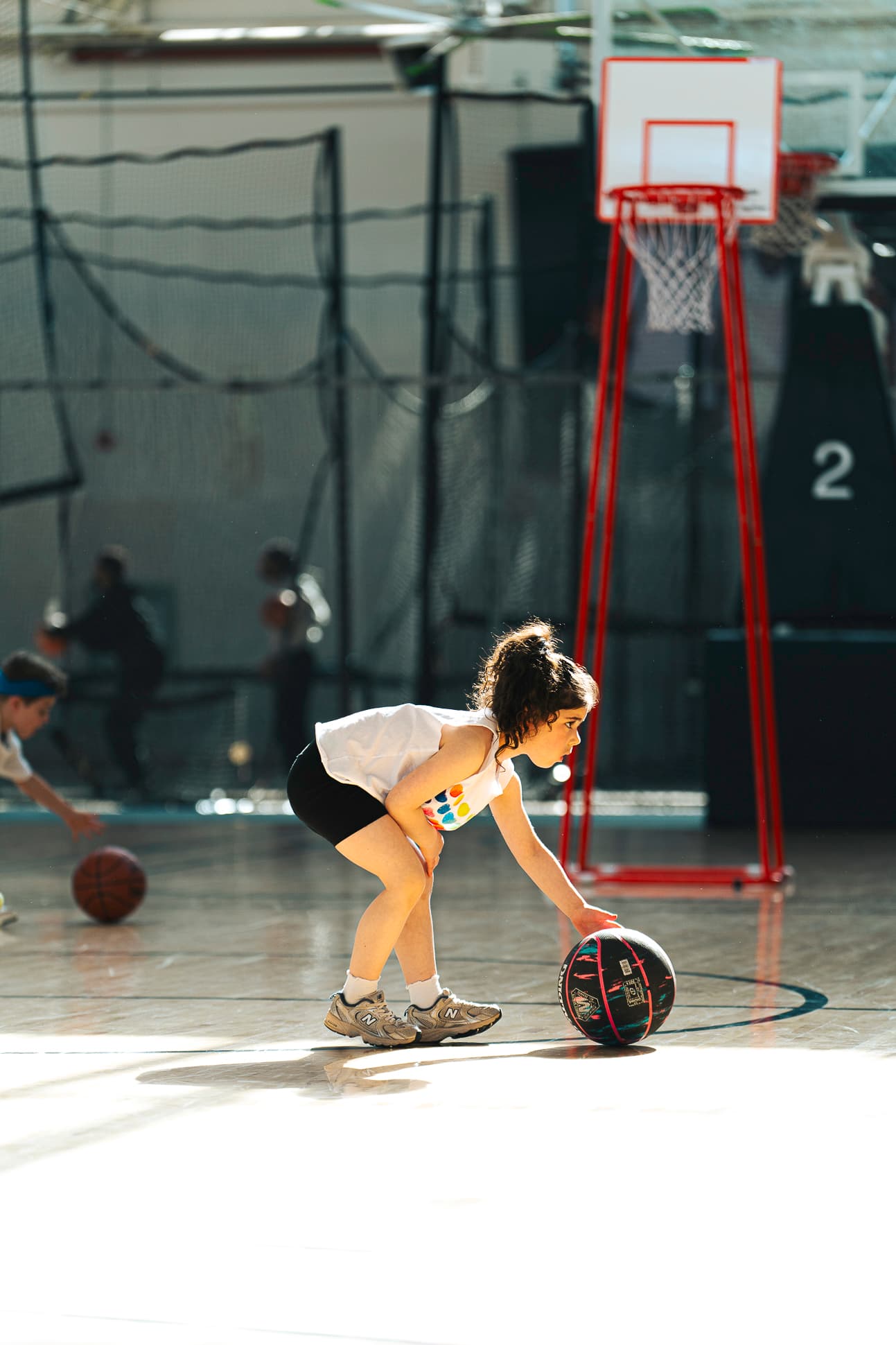 A young athlete bent low over the ball, dribbling beside a portable hoop