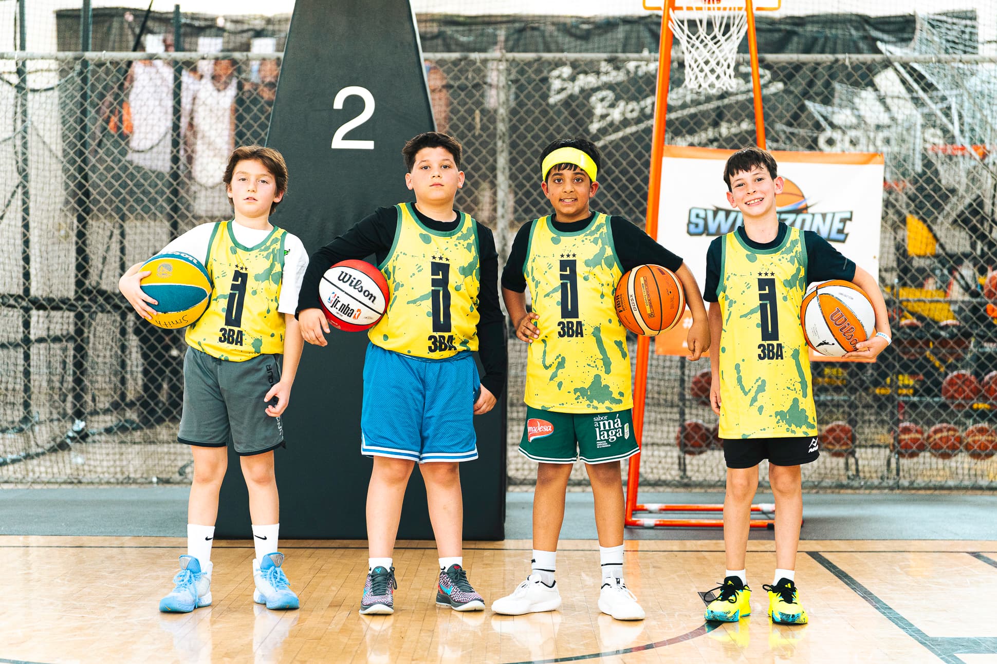 Four young players in yellow 3BA pinnies standing shoulder to shoulder, each holding a basketball